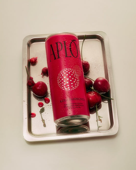 A can of Aplós Kola Fashioned cocktail placed on a tray with cherries around it, with the branding 'APLO' visible on the can.