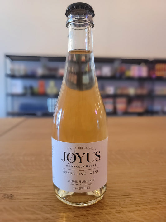 A bottle of Joyus mini Non-Alcoholic Sparkling wine with a label showing the brand and the type of the product. The bottle is placed on a wooden surface.