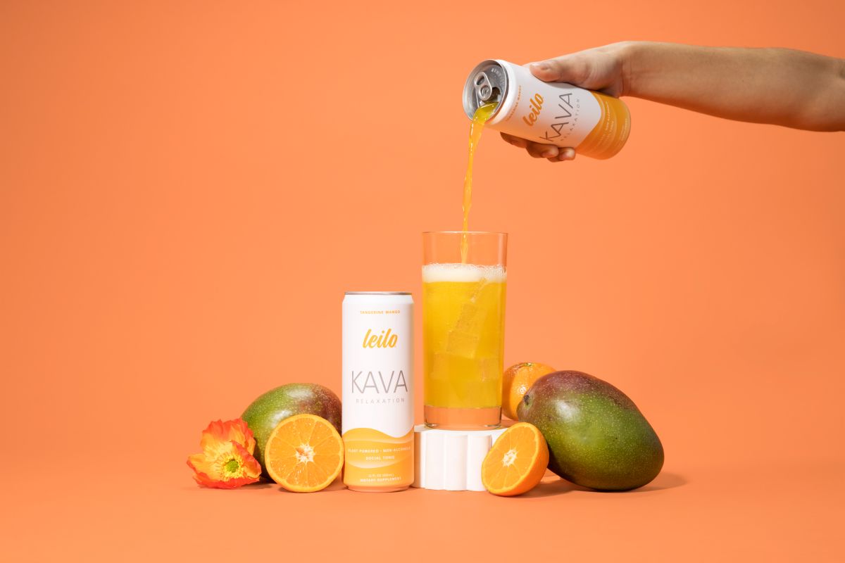 Person pouring KAVA drink into a glass with mangoes and oranges on an orange background