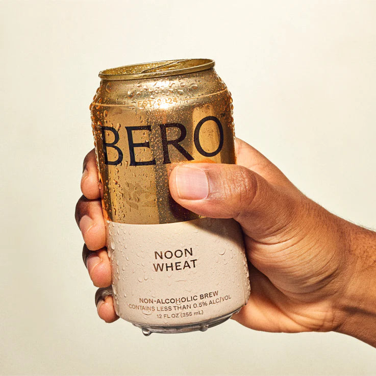 Hand holding a can of BERO Noon Wheat non-alcoholic brew against a plain background
