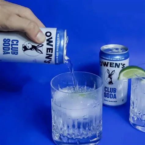Hand pouring Club Soda into a glass with lime wedge, Owen's Club Soda can in the background.