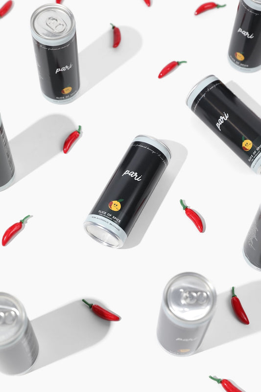 Multiple cans of Pari energy drink arranged on a white background with red chili peppers scattered around.