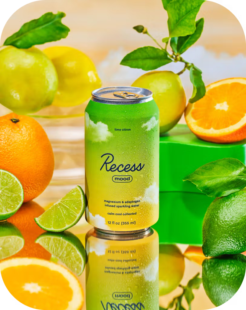 Green can of Recess mood surrounded by citrus fruits on a reflective surface