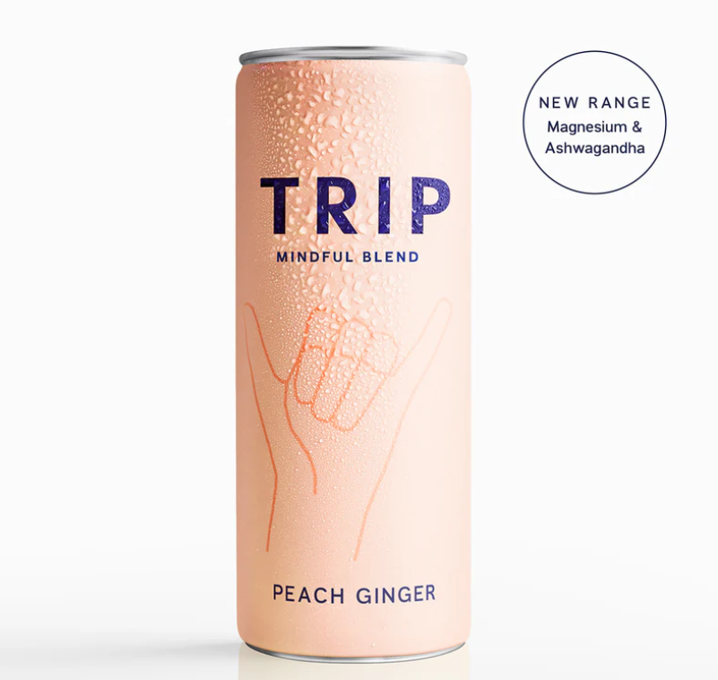 A can of TRIP Mindful Blend Peach Ginger Sparkling Botanical Drink with a pink hue and hand graphics, indicating a new range with magnesium and ashwagandha.