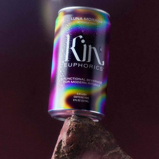 A can of Kin Luna Morada functional beverage placed on a textured surface with a colorful reflective background.