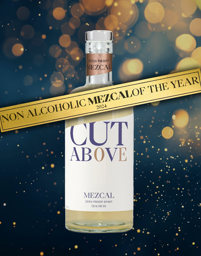 A bottle of Cut Above Zero Proof Mezcal with the text 'NON ALCOHOLIC MEZCAL OF THE YEAR' above it. The bottle is labeled and has a clear liquid inside, presented against a dark background with bokeh lights.