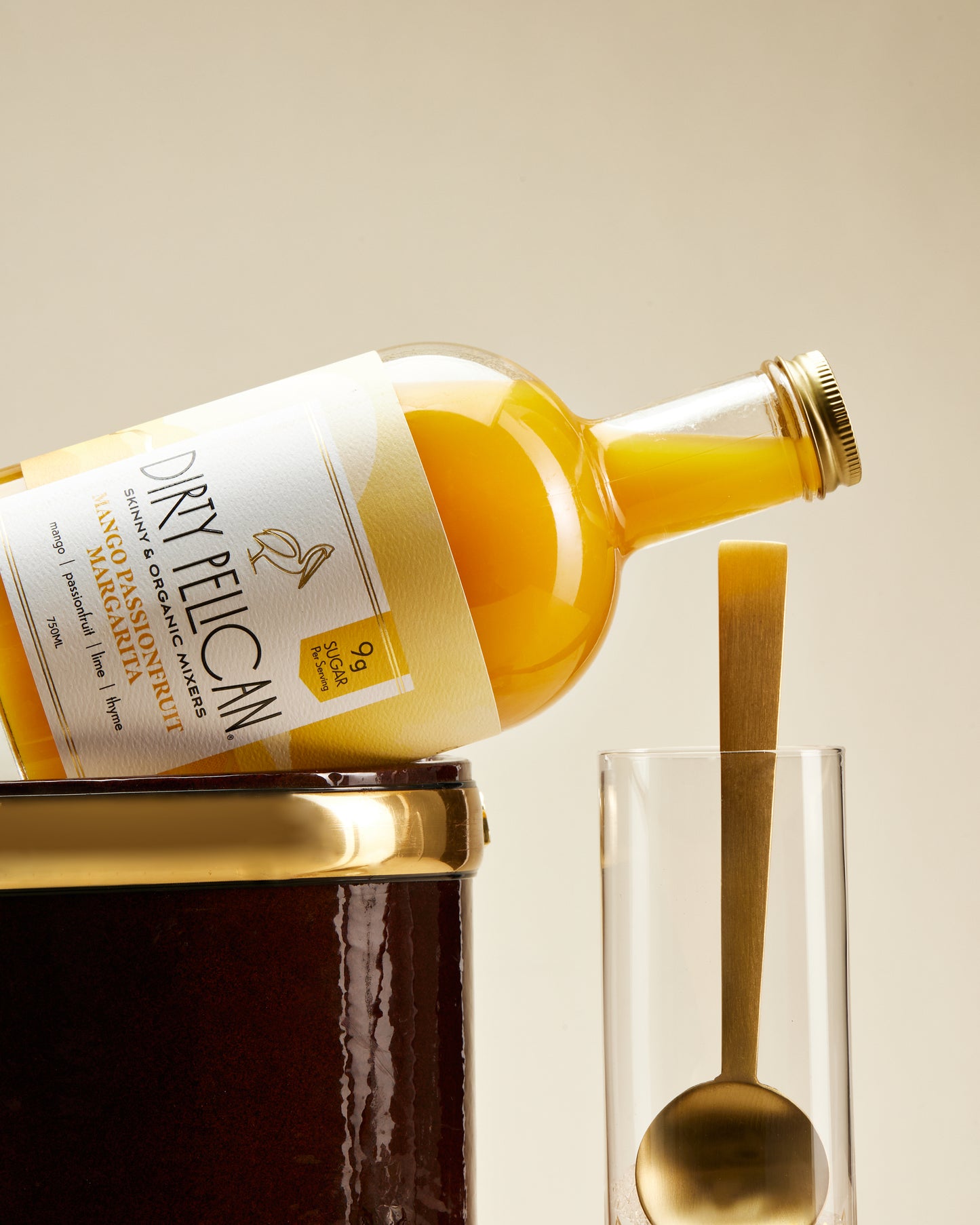 Bottle of Dirty Pelican orange juice being poured into a glass with a spoon on a beige background
