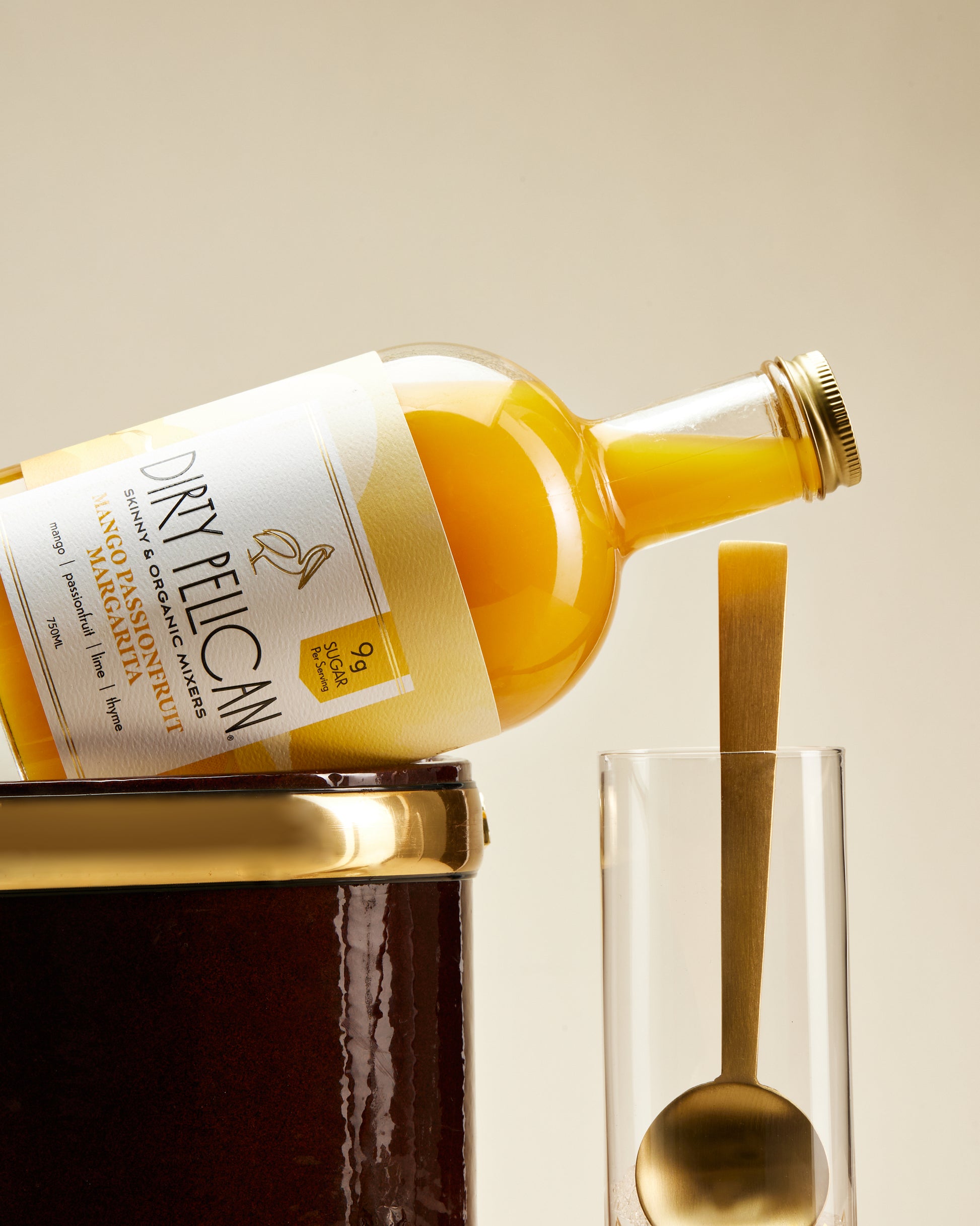 Bottle of Dirty Pelican orange juice being poured into a glass with a spoon on a beige background