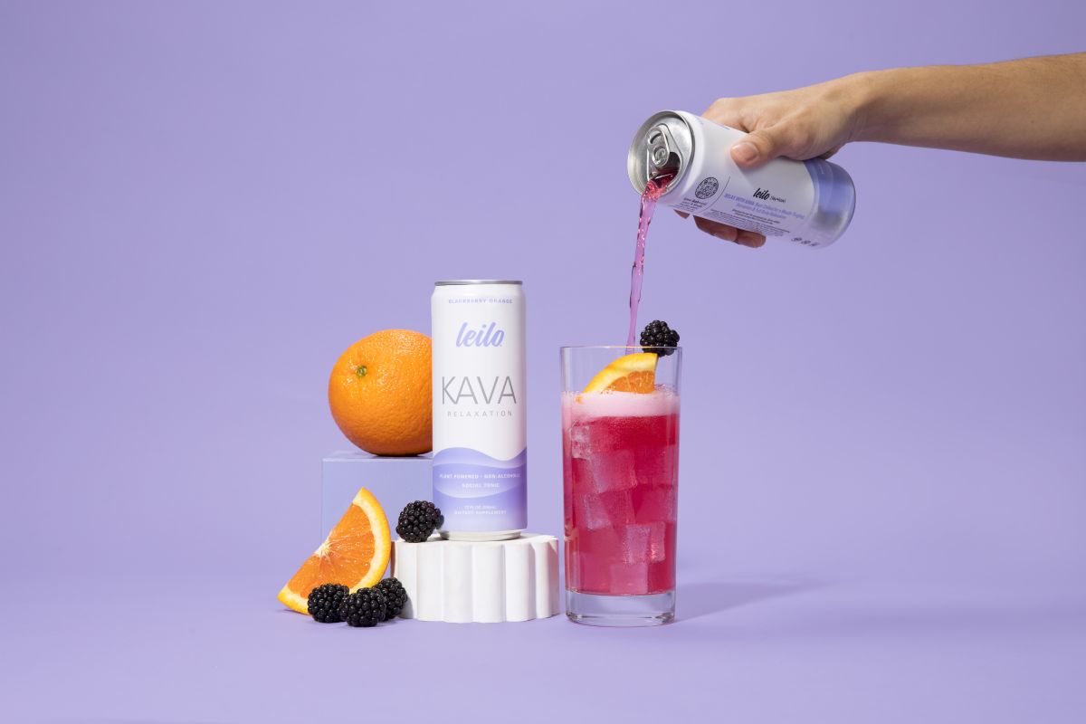 Person pouring Kava drink from a can into a glass with fruit on a purple background