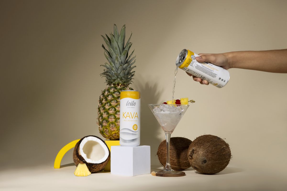 Person pouring Kava drink into a cocktail with pineapple, coconut, and banana on a beige background