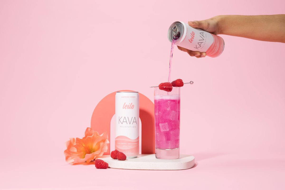 Person pouring pink Kava drink from a can into a glass with raspberries on a pink background