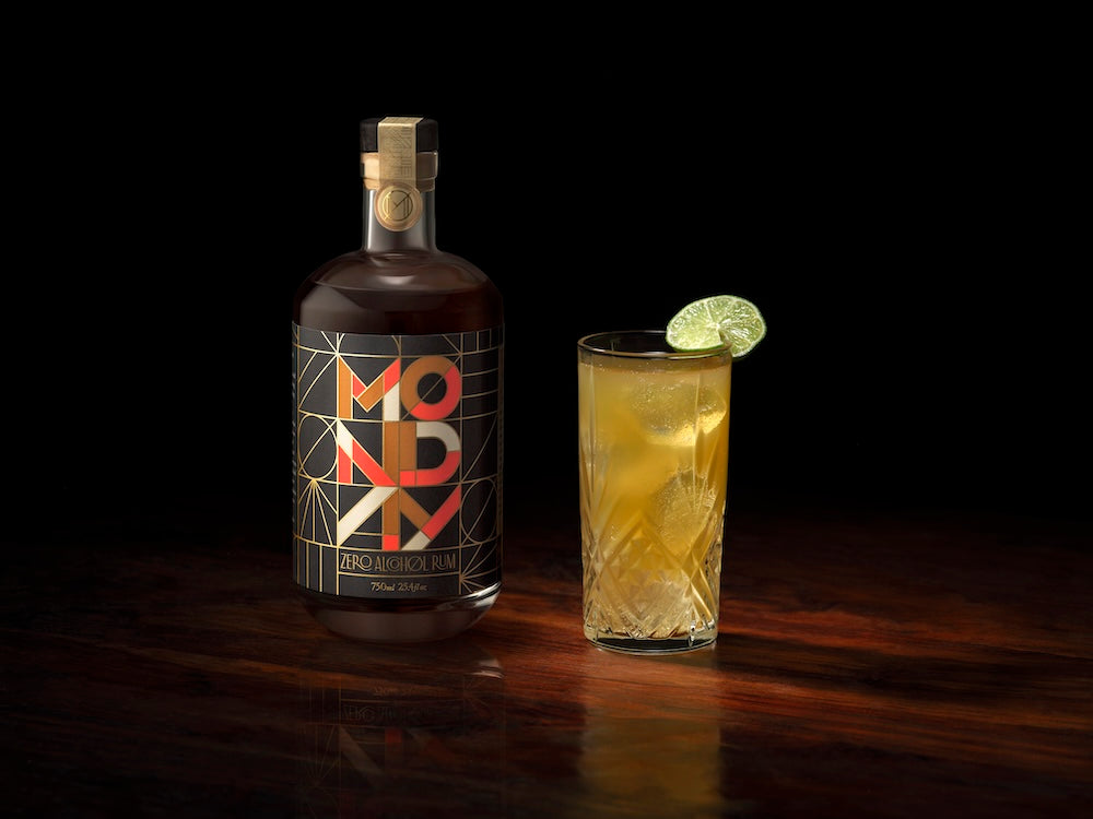 A bottle of Monday Zero Alcohol Rum with a glass of mocktail next to it, both with a slice of lime on the glass.