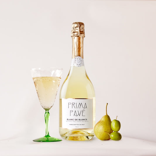 A bottle of Prima Pave Blanc de Blancs wine with a glass and some fruits in the foreground.