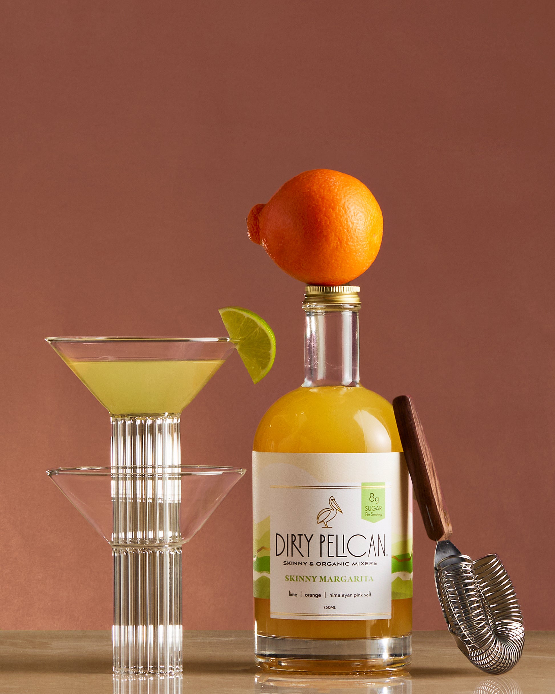 Bottle of Dirty Pelican cocktail with a cocktail glass and bar tools on a brown background