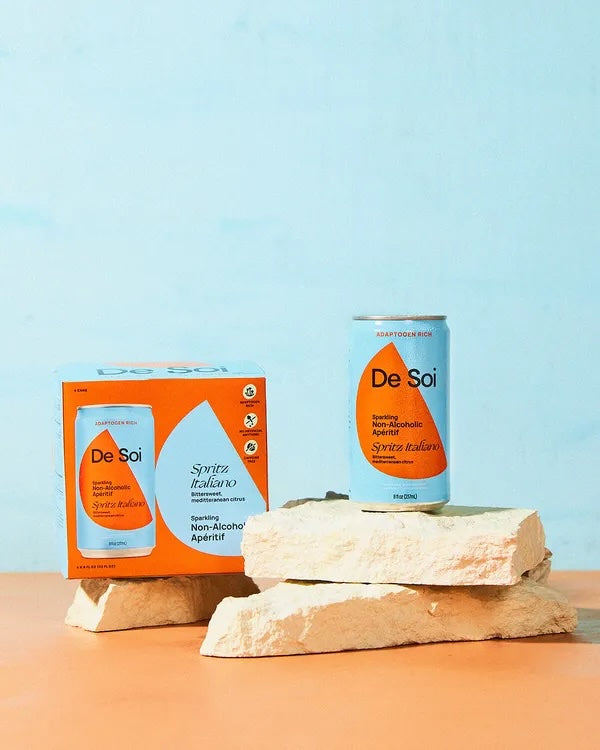 Four cans of De Soi Spritz Italiano are displayed, with two standing upright and two leaning against a block of ice. The packaging is predominantly white with orange accents, and the text indicates it is a product with 'Mediterranean Citrus' flavor.