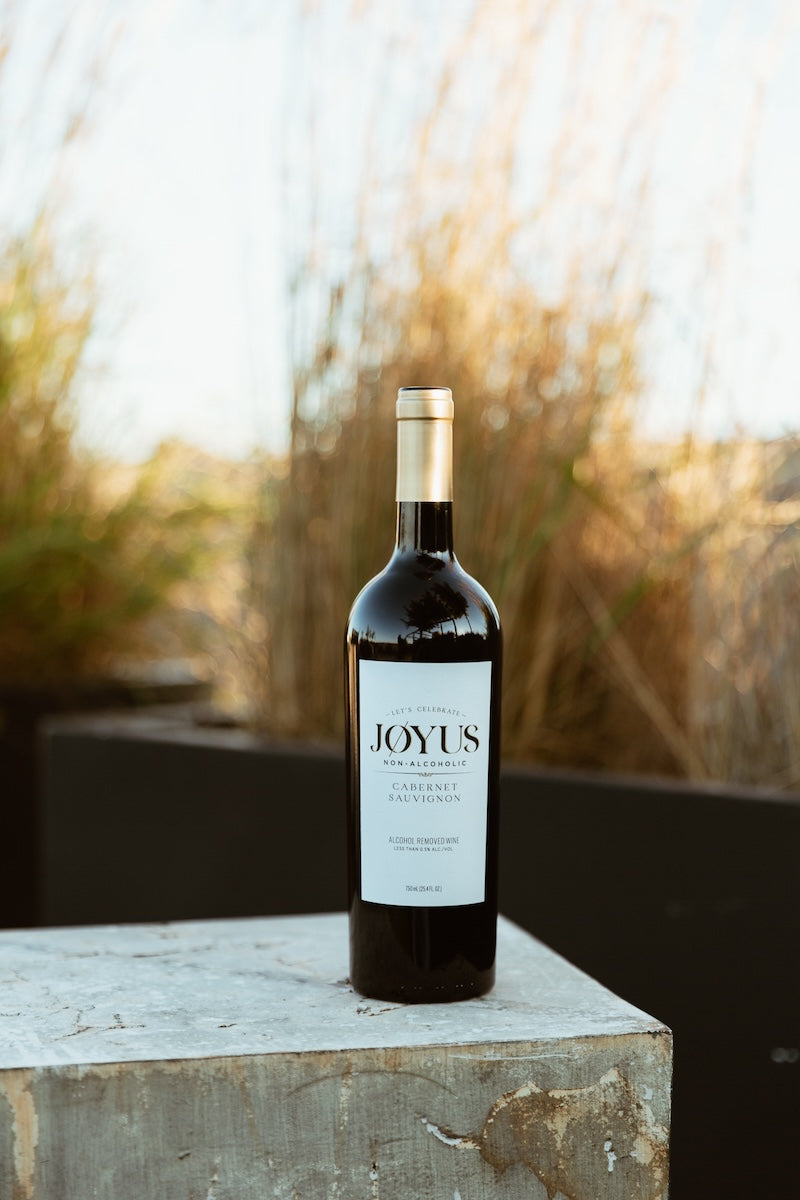 A bottle of Joyus Non-Alcoholic Cabernet Sauvignon red wine placed on a concrete block with a natural background.