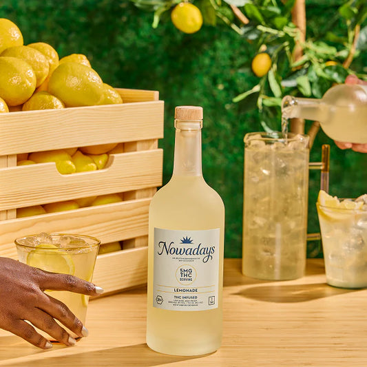 Bottle of 'Nowadays' lemonade with lemons and a glass on a wooden table.