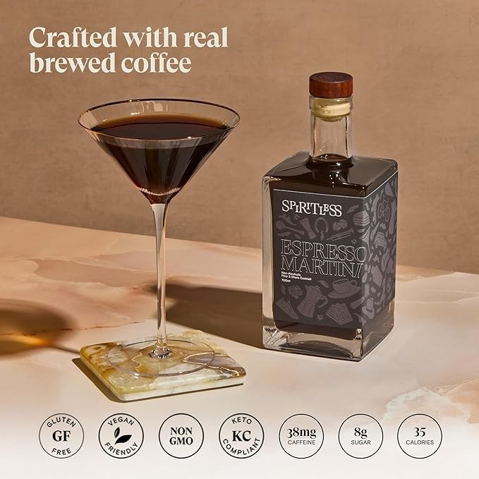 A bottle of Spiritless Espresso Martini next to a filled martini glass on a coaster, with the bottle having a dark label and the glass displaying a dark brown liquid.